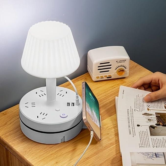 White desk lamp with multiple outlets on a wooden surface, with a phone and magazine nearby.