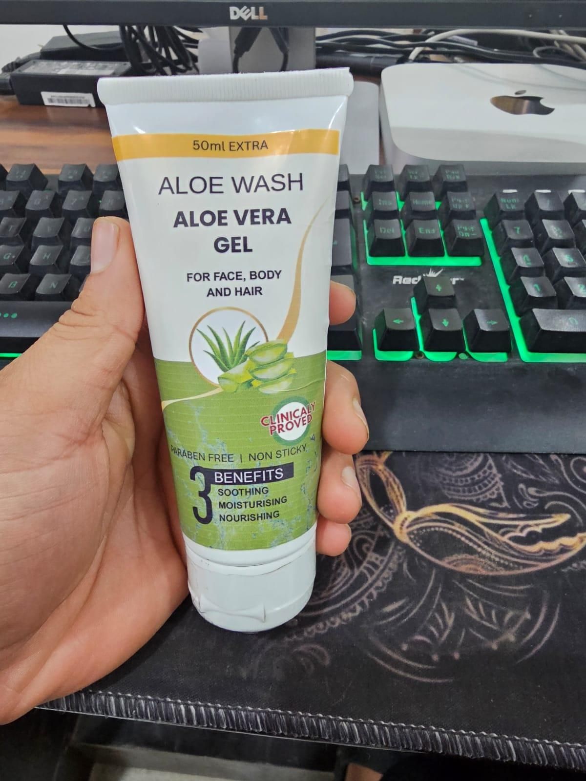 Hand holding a tube of Aloe Vera gel in front of a computer keyboard