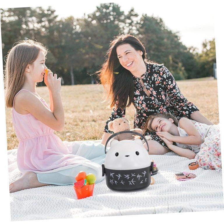 Woman and two children sitting on a blanket outdoors with a plush toy and fruit.