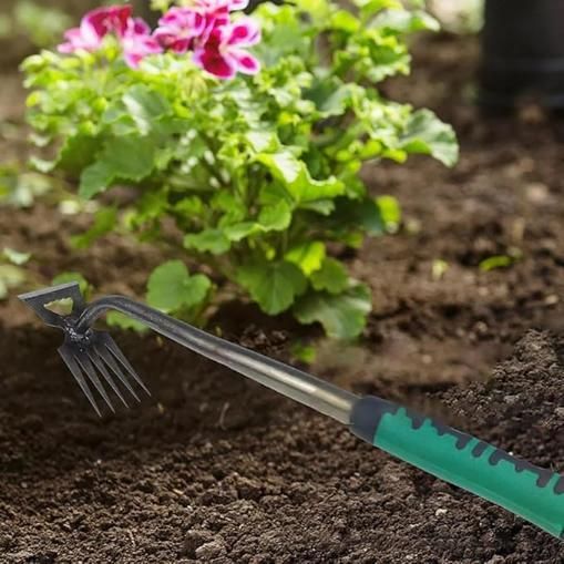 Gardening tool with green handle in soil next to a plant with pink flowers