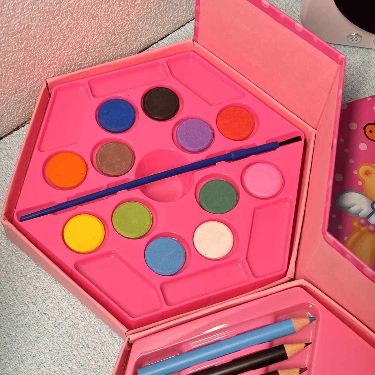 Pink children's art set with watercolor paints and brushes on a textured surface.