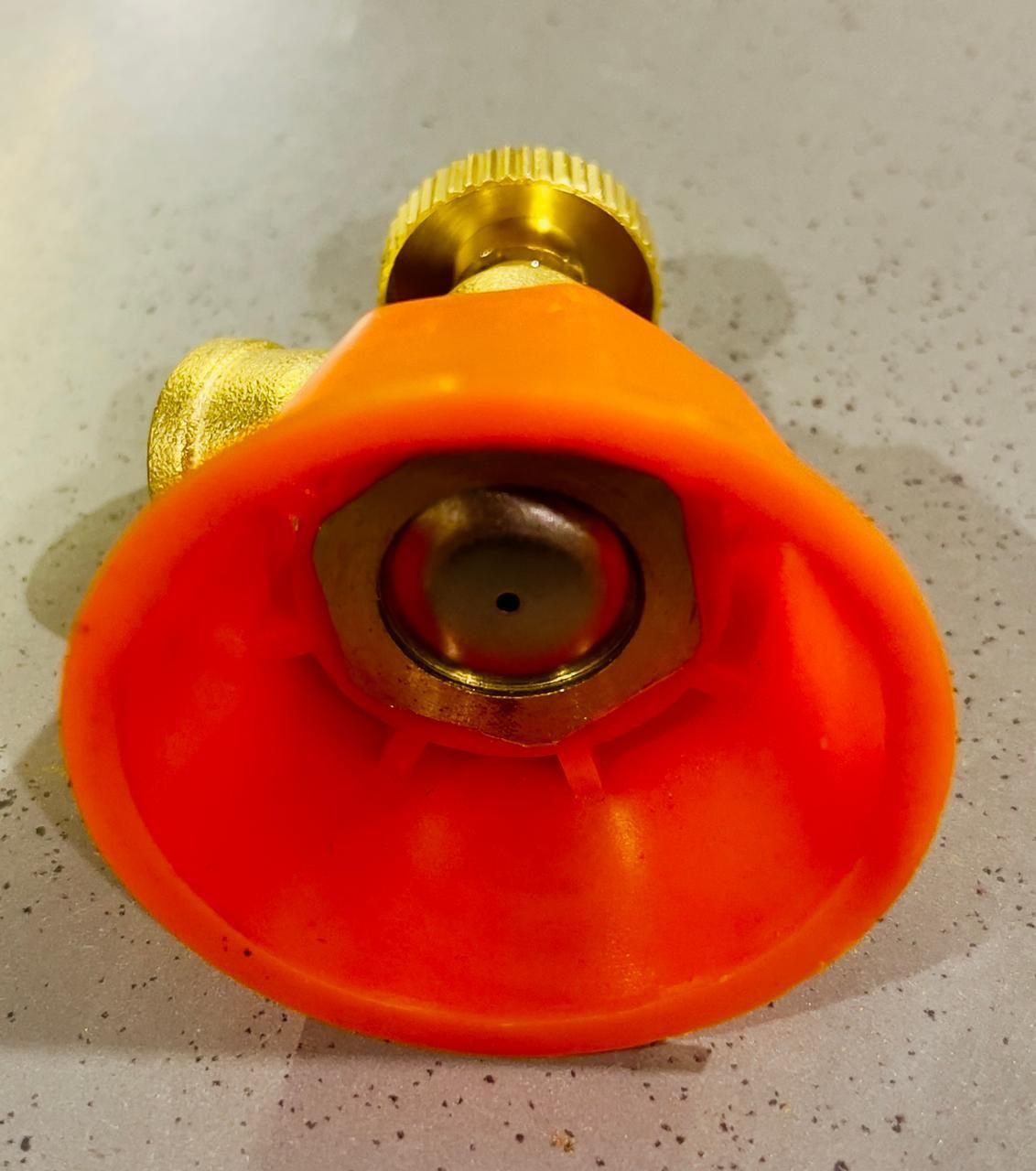 Orange spray nozzle with gold-colored valve on a speckled surface