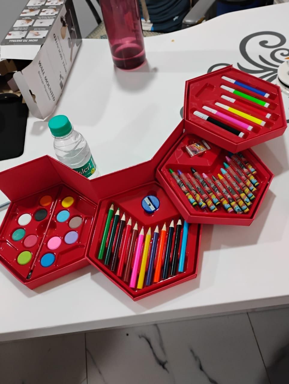 Red art set with pencils, watercolors, and other tools on a white table.