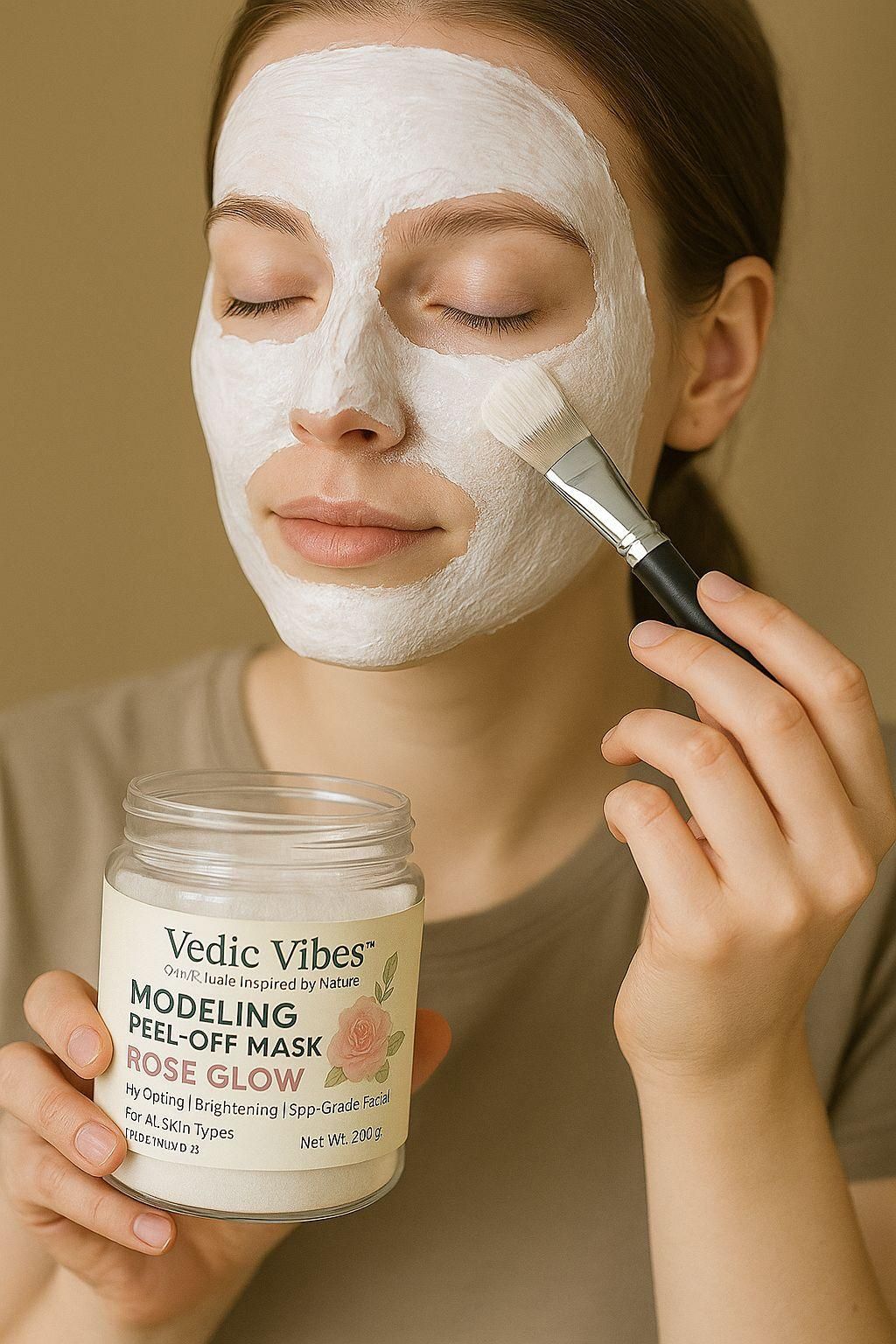 Person applying a white facial mask with a brush, holding a jar labeled 'Vedic Vibes' against a beige background.